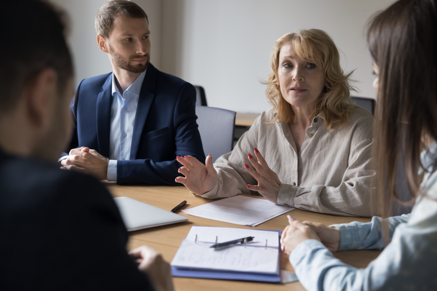 An older woman in outlining a point sitting next to her colleagues at a conference table.