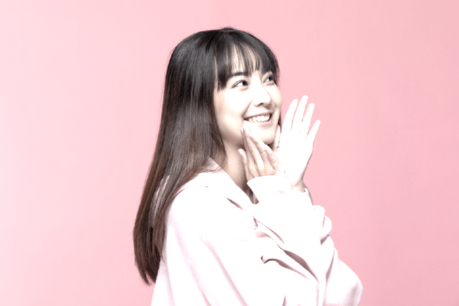 Young woman posing for a picture with her hands under her chin.