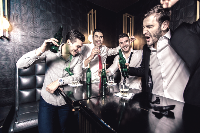 Four men in a bar with drinks in front of them, appearing animated.