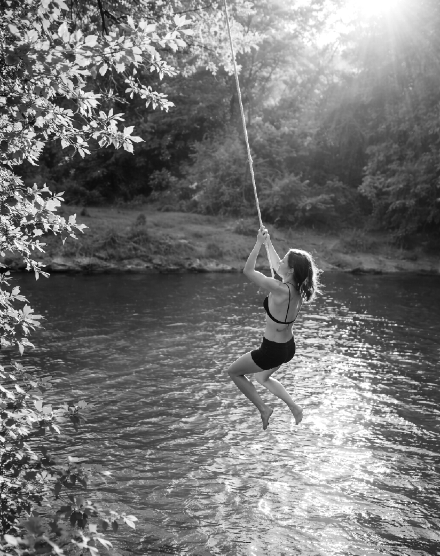 A teenage girl swinging from a rope over a river, midair above the water on a warm summer afternoon.