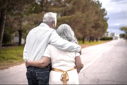 gray-haired older couple, arm-in-arm walking on the road during daytime