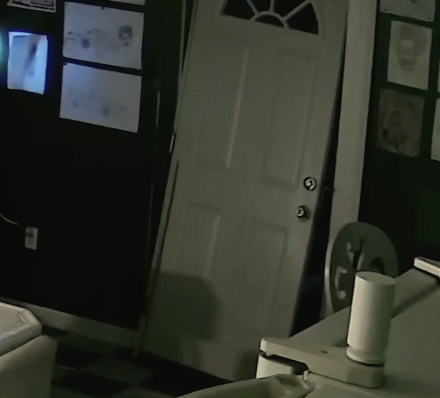 Security-camera still showing a broken front door hanging off-center inside Afroman’s home after the raid.