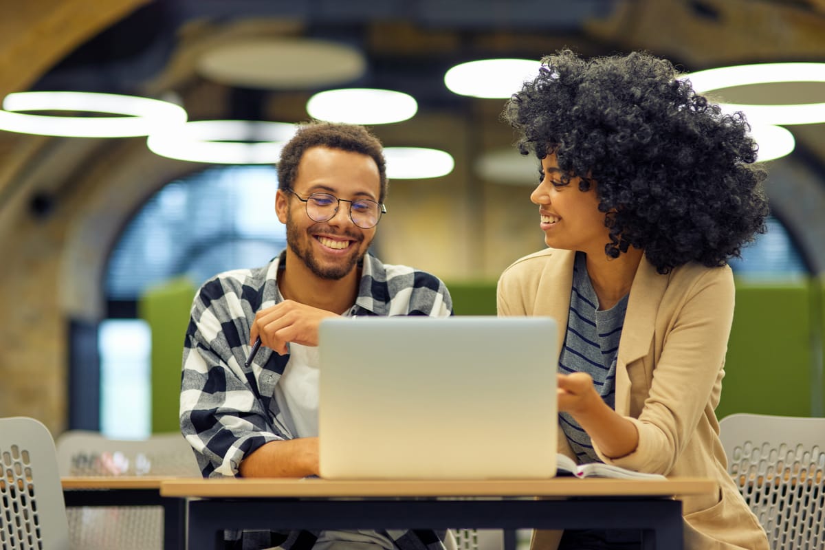 two smiling colleagues near a single computer, showcasing teamwork.