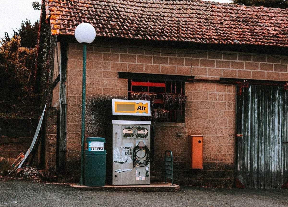A standalone tire air compressor next to a small building, weathered and unattended.