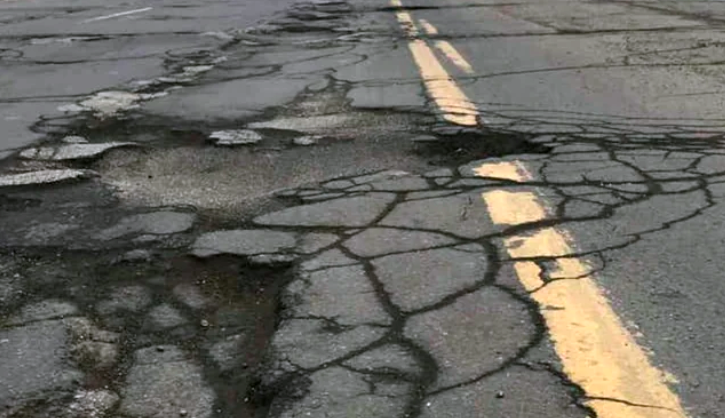 Cracked asphalt roadway with multiple potholes and fractures crossing a faded yellow center line.