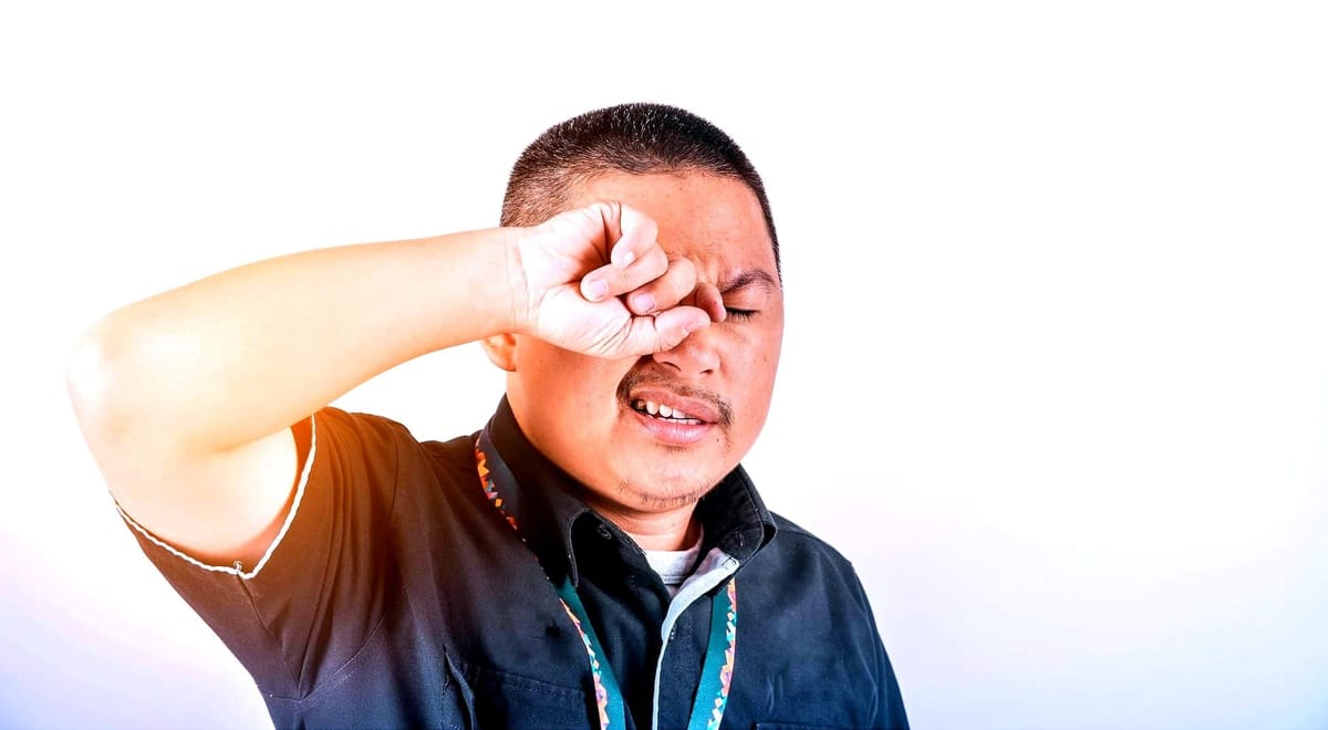 A person rubs their eyes in frustration against a bright white background.