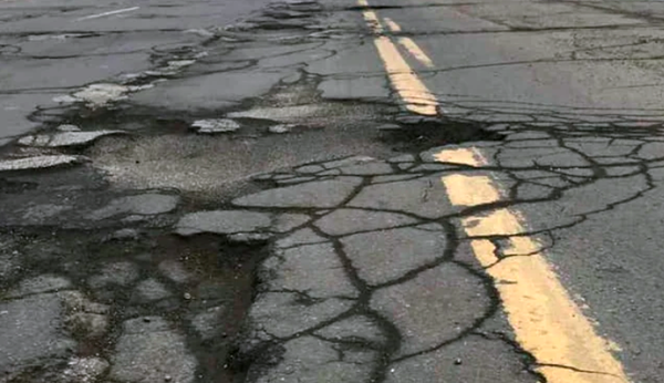 Cracked asphalt roadway with multiple potholes and fractures crossing a faded yellow center line.