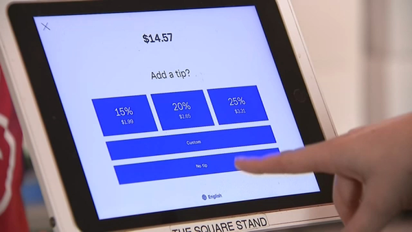A checkout screen asks whether  you want to tip 15%, 20%, 25%, custom or no tip. A finger points at the screen.